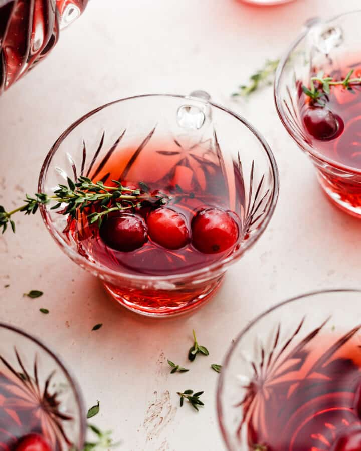 Close-up of a glass of cranberry rum punch garnished with thyme and fresh cranberries.