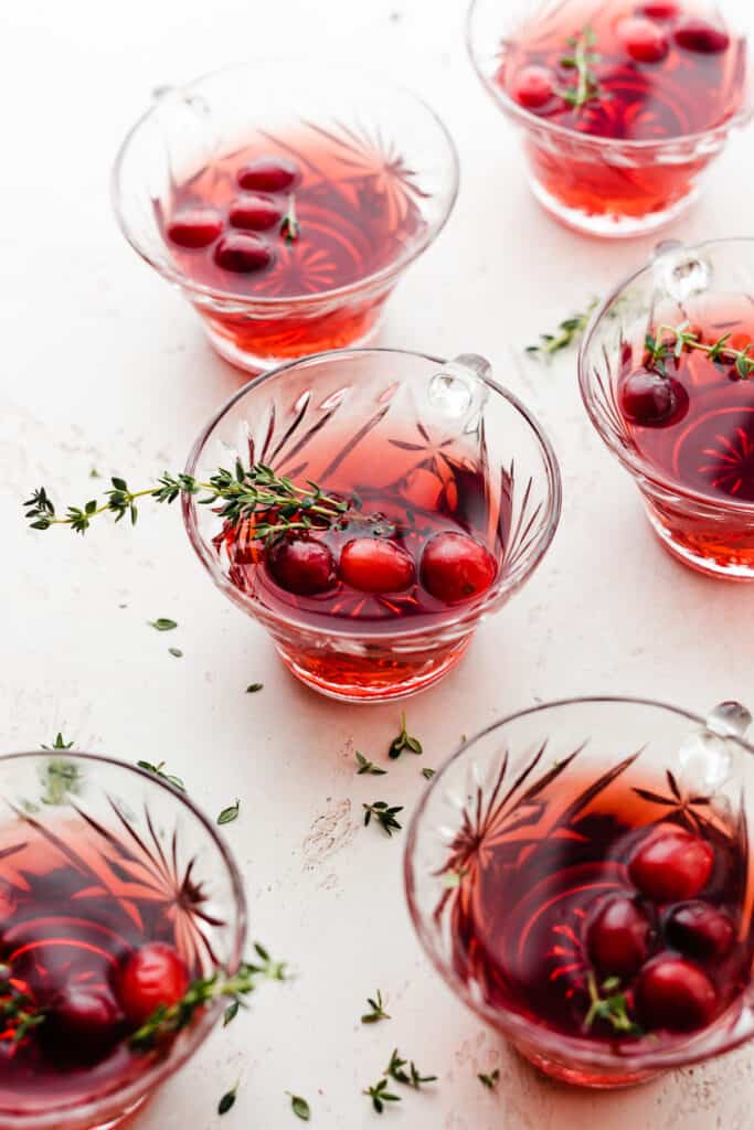 6 glasses of cranberry rum punch garnished with fresh cranberries and thyme.