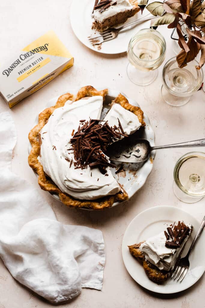 An overhead shot of the sliced french silk pie with slices of pie on plates. The pie is topped with whipped cream and chocolate curls.