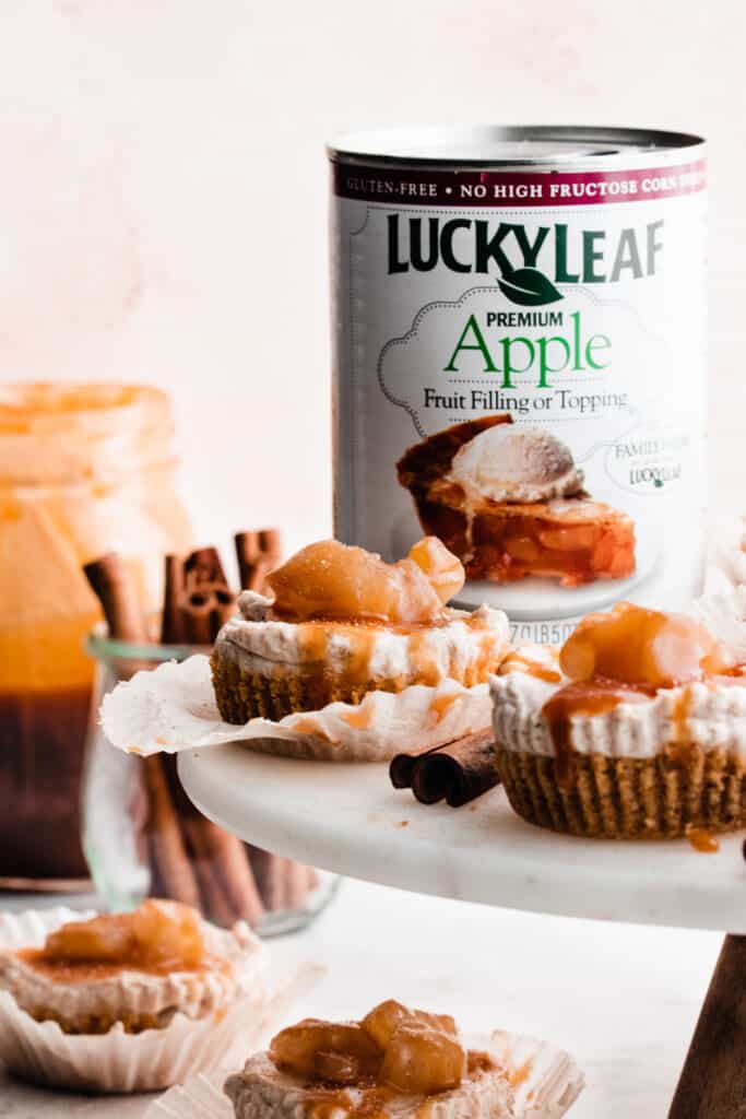 Mini apple pie cheesecakes on a marble cake stand with a can of lucky leaf apple fruit filling in the background.