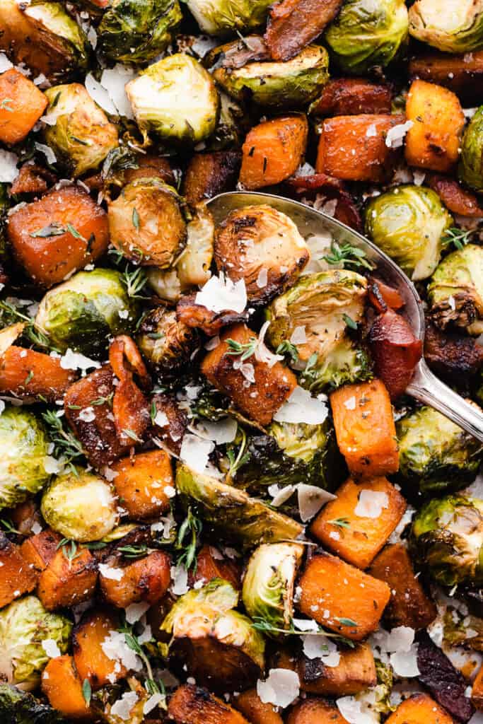 A close-up of a spoon scooping into the roasted veggies and bacon.