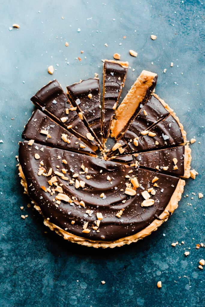 A sliced peanut butter chocolate tart garnished with peanut pieces and flaky salt.