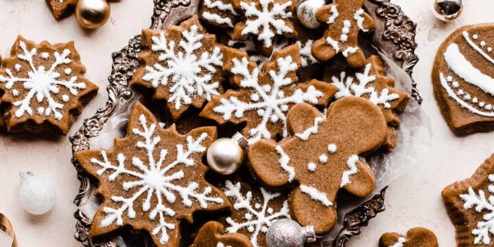 Gingerbread cookies piped with royal icing, in a silver tray surrounded by gold ribbon and mini ornaments.