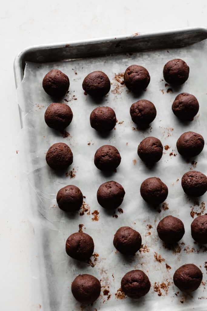 A baking sheet lined with wax paper and filled with rows of plain chocolate truffles.