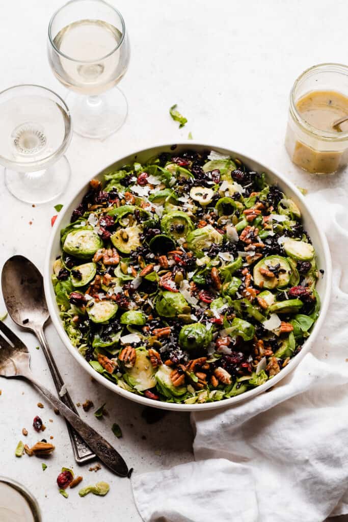 A bowl of brussels salad with a jar of dressing.
