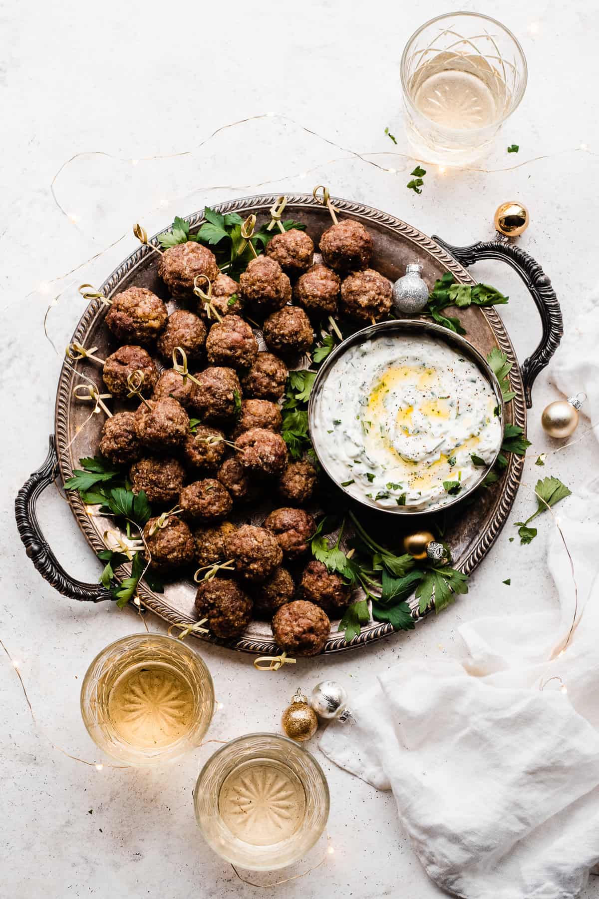 A platter of meatballs on skewers, with a bowl of yogurt dip and glasses of wine.