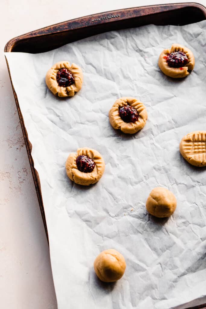 A baking sheet with cookie dough balls, and crisscross preserve filled cookies.
