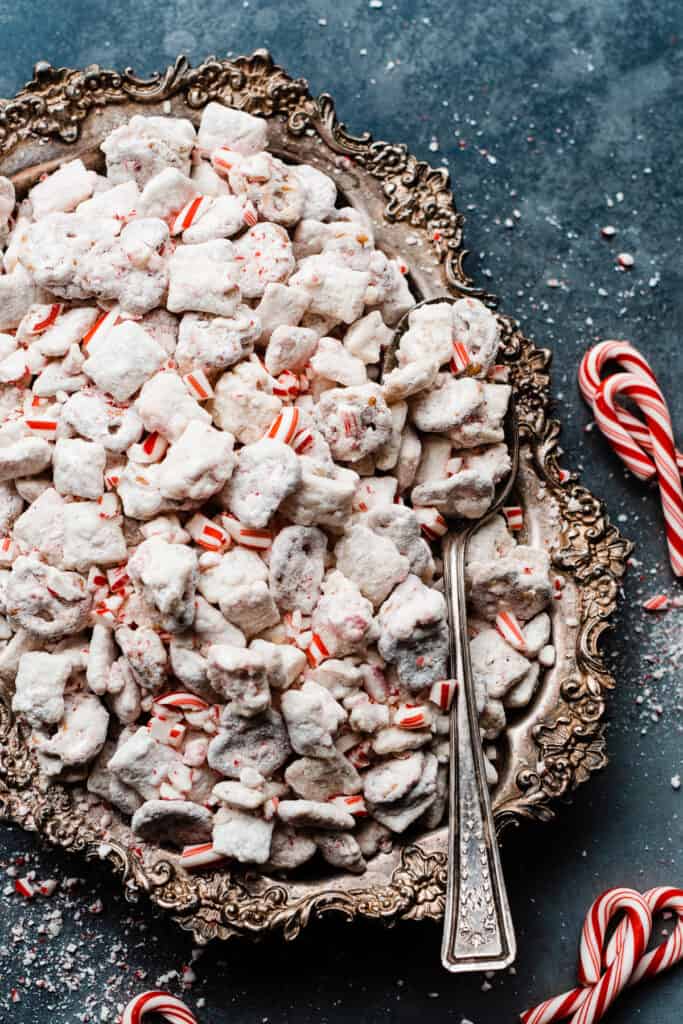 A vintage tray of white chocolate peppermint puppy chow on a blue surface, with candy canes scattered around.