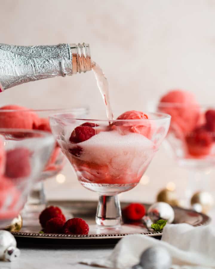 Sparkling champagne being poured over raspberry sorbet in a glass.