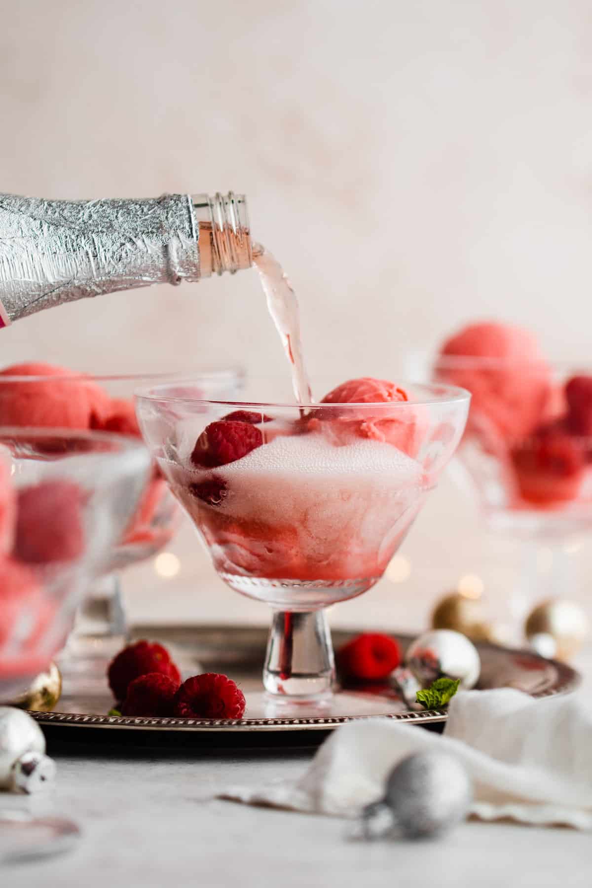 Sparkling champagne being poured over raspberry sorbet in a glass.