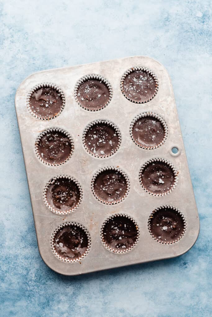 Chilled peanut butter cups in a muffin tin, topped with flaky sea salt.