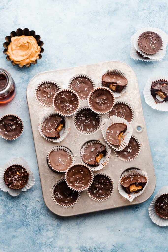 Peanut butter cups in a mini muffin tin and scattered around, on a light blue surface.