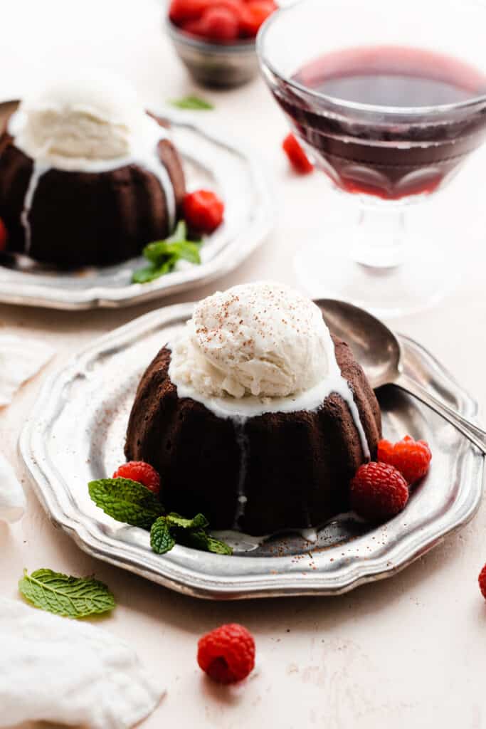 Two plates of chocolate lava cakes topped with ice cream and fresh raspberries.