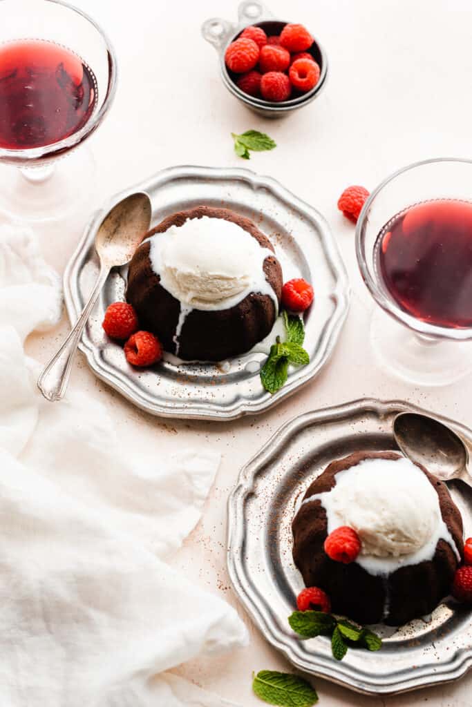 Two plates with a chocolate lava cake on each one, topped with ice cream and fresh berries.