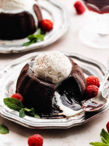 A chocolate lava cake on a plate, topped with ice cream and raspberries, with the molten center spilling out.