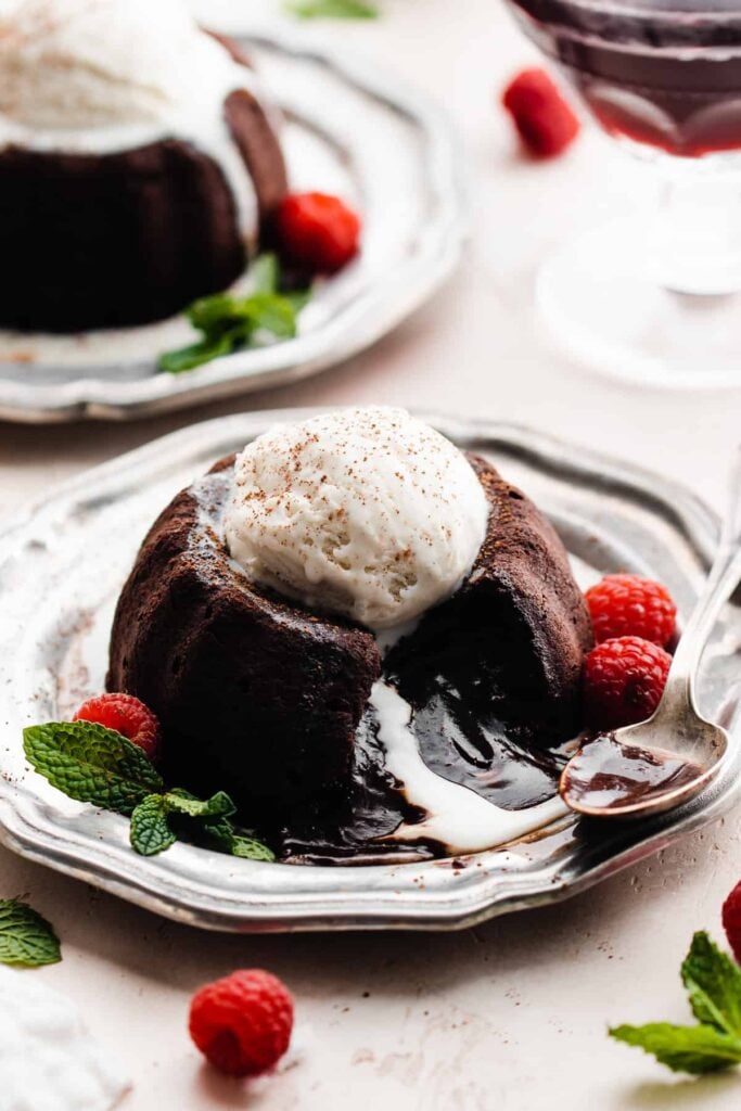 A chocolate lava cake on a plate, topped with ice cream and berries, with a pool of chocolate spilling out.