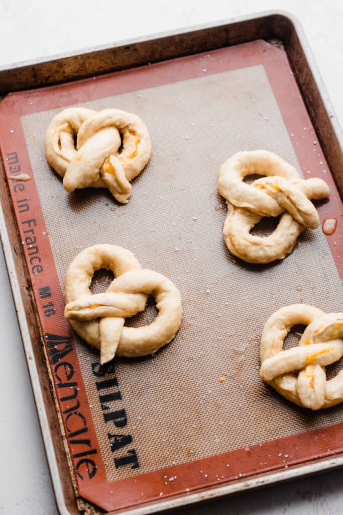 A baking sheet with unbaked pretzels that have been baking soda bathed and egg washed.