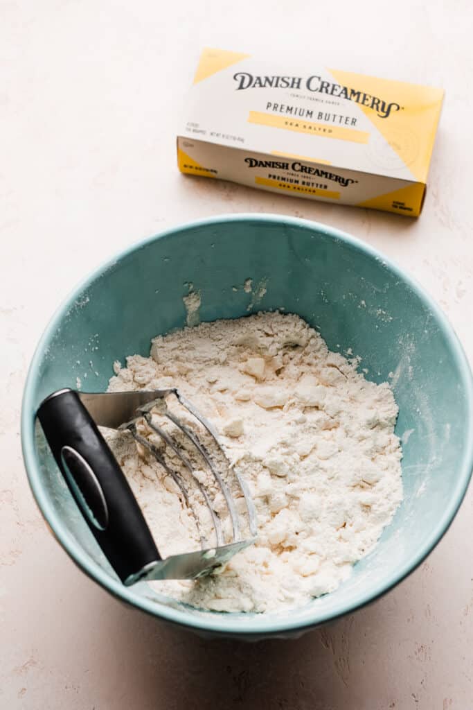 A bowl of butter being cut into the flour with a pastry cutter.