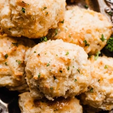 A close-up of the drop biscuits in a serving tray, brushed with melted butter and sprinkled with sea salt and parsley.