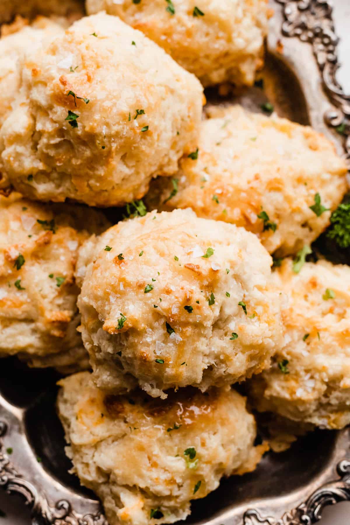 A close-up of the drop biscuits in a serving tray, brushed with melted butter and sprinkled with sea salt and parsley.
