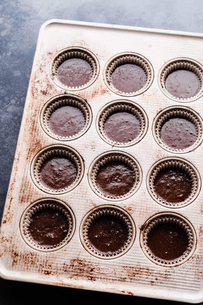 A cupcake pan with liners filled 2/3 of the way full of batter.