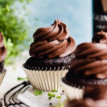 A close-up of a chocolate cupcake with a big swirl of frosting, with clovers scattered around.