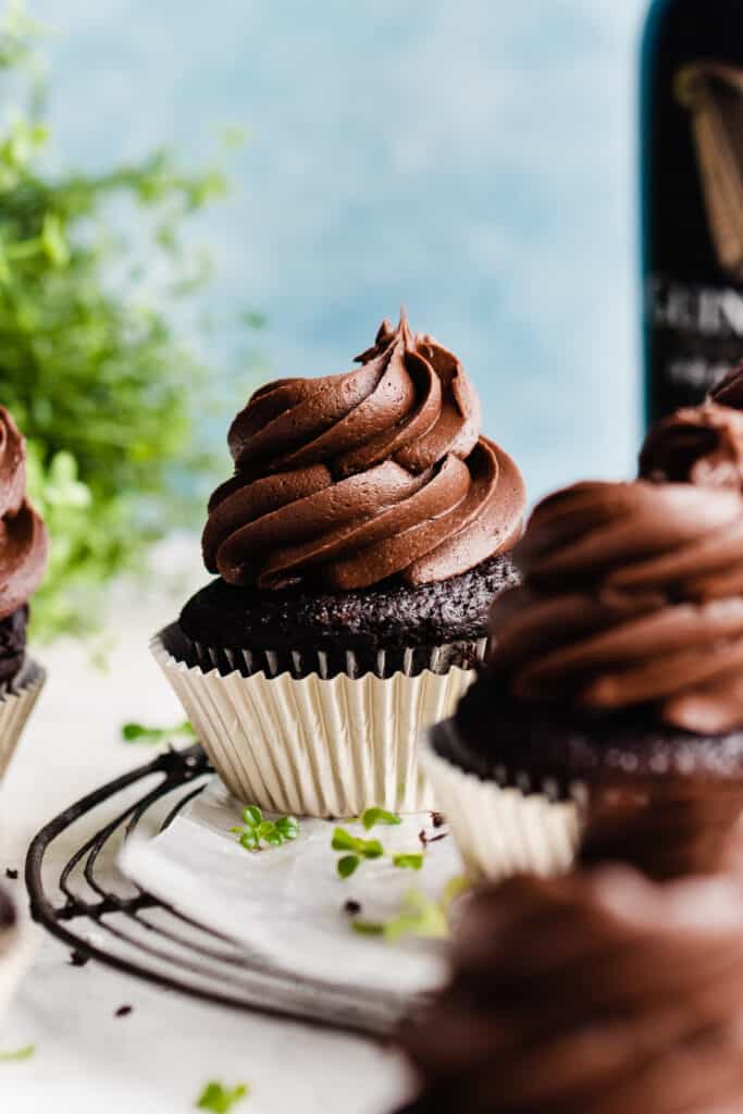 A close-up of a guinness chocolate cupcake topped with a swirl of chocolate frosting, with clovers scattered around.