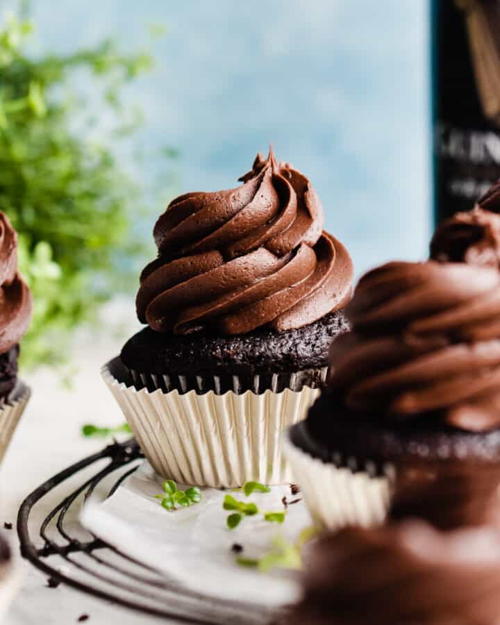 A close-up of a chocolate cupcake with a big swirl of frosting, with clovers scattered around.