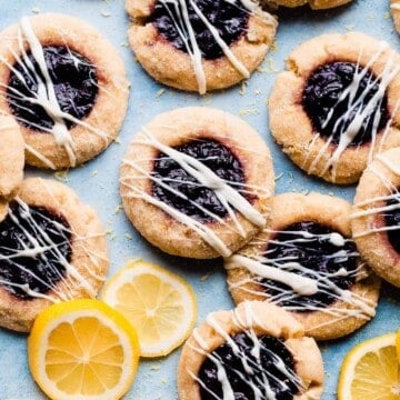 White chocolate drizzled lemon blueberry sugar cookies on a blue surface.