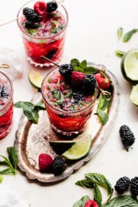 Three glasses of mixed berry mojitos garnished with fresh berries and mint.