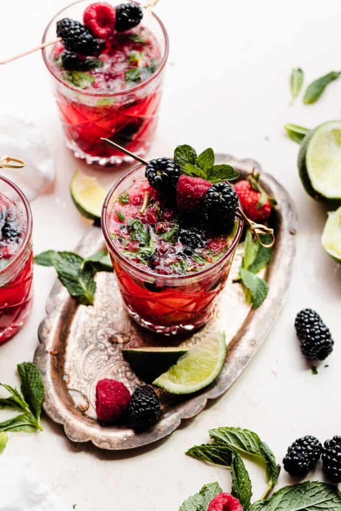 Three glasses of mojitos topped with blackberries, raspberries, and fresh mint.