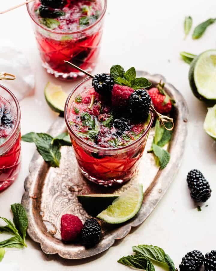 Three glasses of mixed berry mojitos garnished with fresh berries and mint.