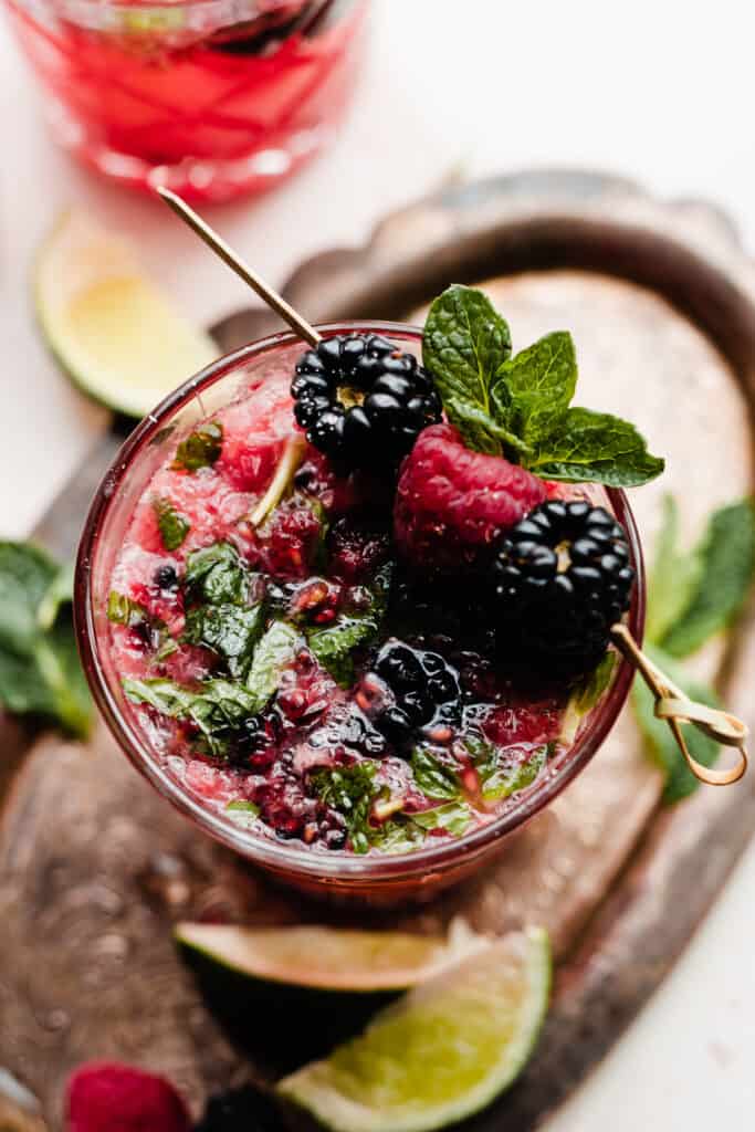 A top-down close up of a brightly colored mojito, garnished with blackberries, raspberries, and mint.