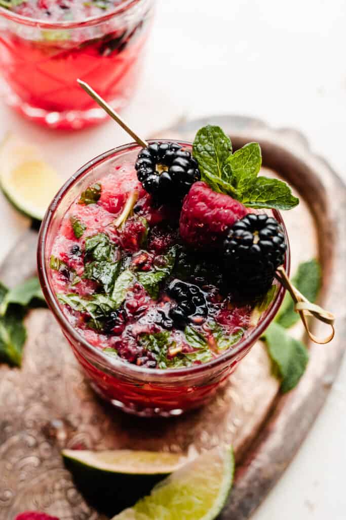 A close-up of a berry mojito, topped with fresh blackberries, raspberries, and mint.