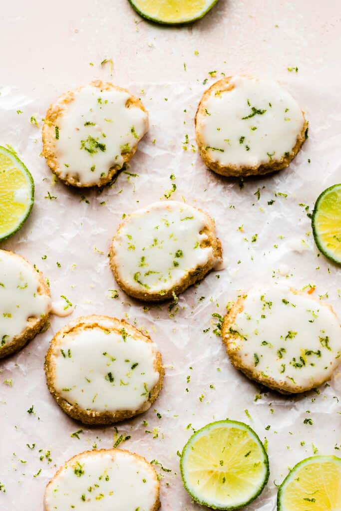 Key Lime shortbread cookies topped with a lime glaze on a light pink surface.