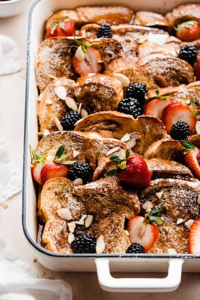 Baked french toast casserole in a pan with fresh berries and powdered sugar.