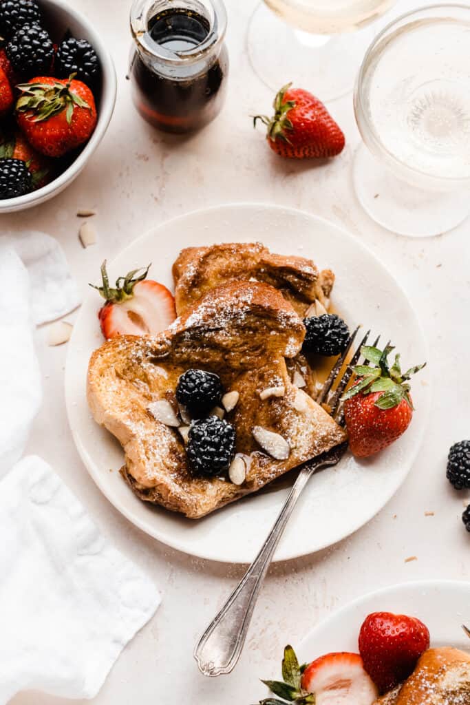 A plate of the french toast served with berries, maple syrup, and powdered sugar.
