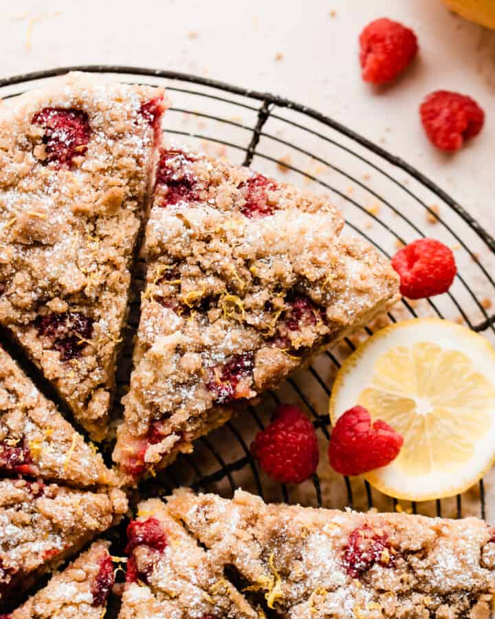 Slices of the crumb cake on a cooling rack with lemons and raspberries scattered around.