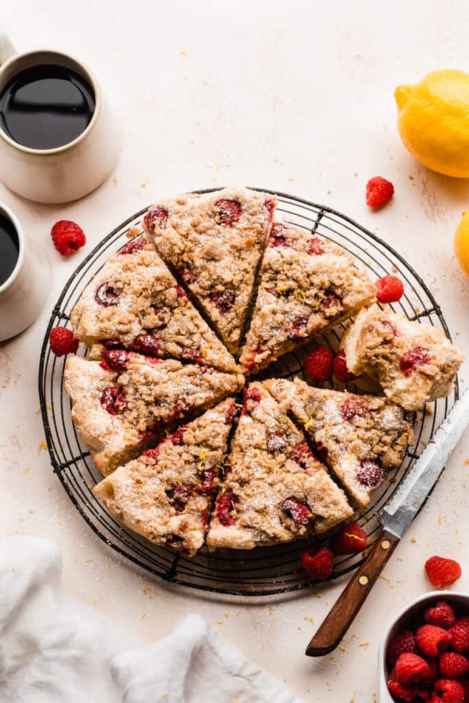 Sliced crumb cake on a cooling rack, with cups of coffee and fresh raspberries.