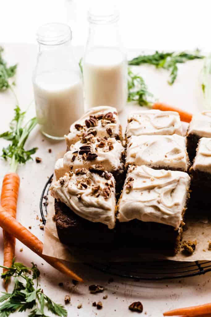 A straight-on view of the sliced carrot cake, with carrots and bottles of milk nearby.