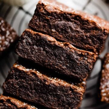 A stack of fudgy brownies with crackly tops and a dusting of powdered sugar.
