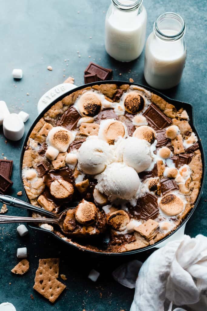 A s'mores skillet cookie topped with toasted marshmallows, melty hershey's chocolate, graham cracker pieces, and scoops of ice cream.