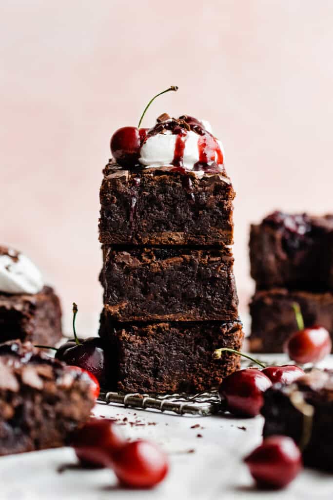 A stack of chocolate brownies swirled with cherry sauce and topped with whipped cream and a cherry.