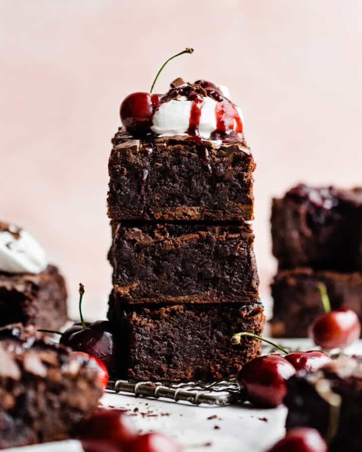 A stack of black forest brownies topped with whipped cream and cherry sauce.