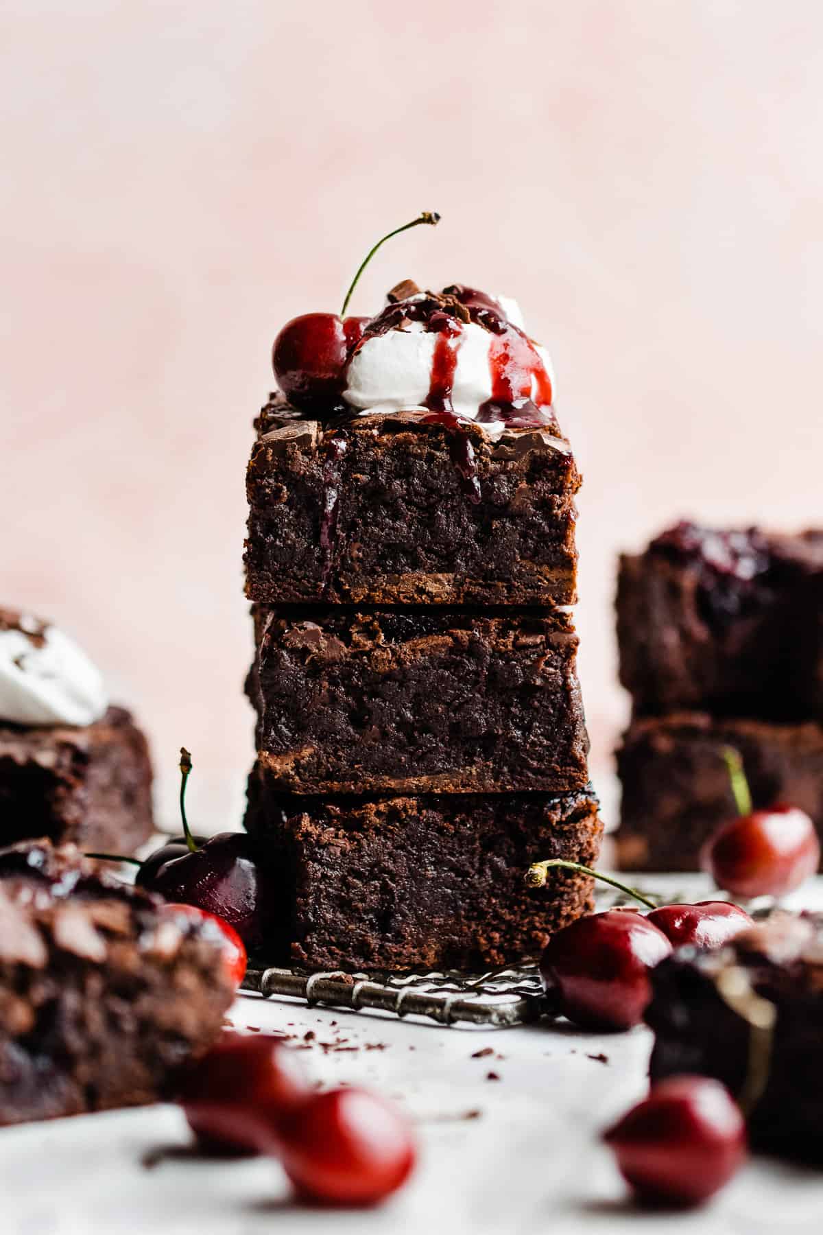 A stack of black forest brownies topped with whipped cream and cherry sauce.