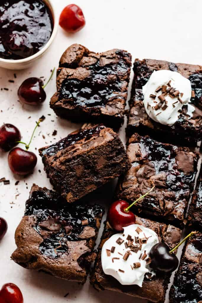 The sliced brownies topped with whipped cream, fresh cherries, and chocolate shavings.