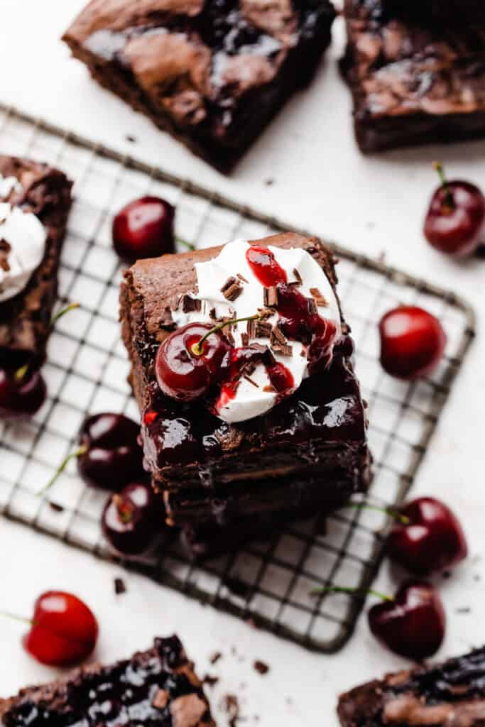 A bird's eye view of a stack of the brownies, with whipped cream and cherry sauce on top and fresh cherries scattered around.