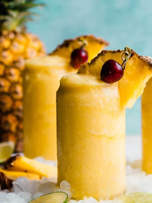 A close-up of a bright yellow piña colada topped with a pineapple wedge and cherry.