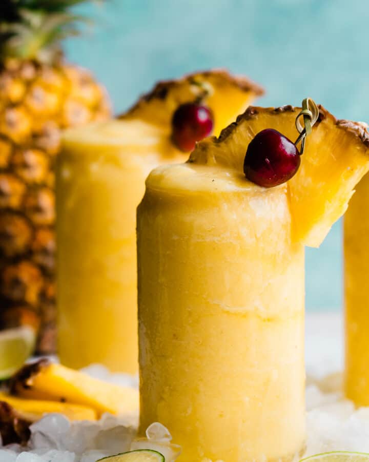 A close-up of a bright yellow piña colada topped with a pineapple wedge and cherry.