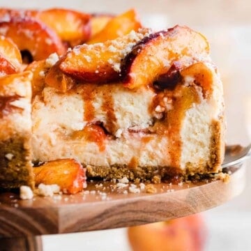 A close-up of a slice of peach cobbler cheesecake with cinnamon peach juice dripping down.